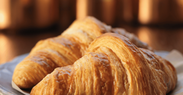 Croissants dorés et croustillants posés sur une grille de refroidissement, accompagnés d’un bol de café.