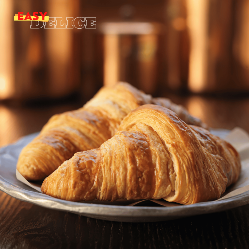 Croissants dorés et croustillants posés sur une grille de refroidissement, accompagnés d’un bol de café.