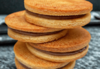 Biscuits sablés dorés, fourrés à la ganache au chocolat, élégamment présentés sur une assiette avec un café fumant.