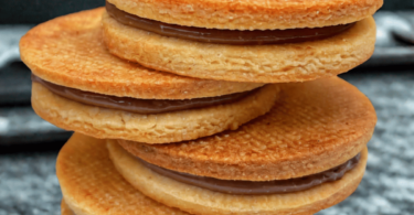 Biscuits sablés dorés, fourrés à la ganache au chocolat, élégamment présentés sur une assiette avec un café fumant.