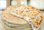 Petits pains dorés à la poêle, garnis de fromage fondant et charcuterie, servis sur une assiette.