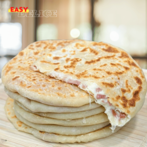 Petits pains dorés à la poêle, garnis de fromage fondant et charcuterie, servis sur une assiette.