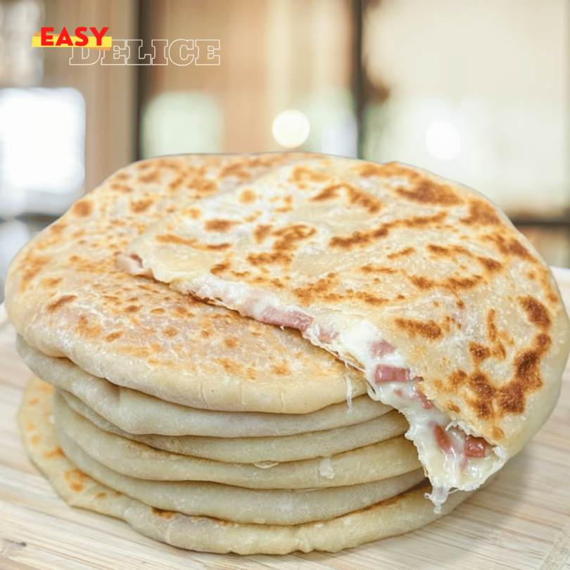 Petits pains dorés à la poêle, garnis de fromage fondant et charcuterie, servis sur une assiette.