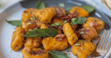 Gnocchis de potimarron dorés, garnis de sauge et de parmesan dans une assiette élégante.