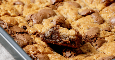 Cookie géant doré, garni de pépites de chocolat et nappé de pâte à tartiner, coupé en parts sur une planche en bois.