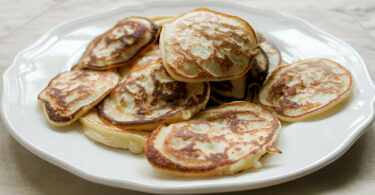 Une assiette de pancakes moelleux à base de banane et œufs, garnis de fruits frais et de miel