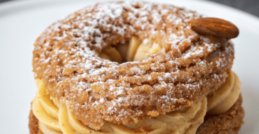 Paris-Brest gourmand avec une garniture de crème pralinée et une décoration d’amandes effilées et de sucre glace