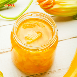 Pot de confiture de courgettes maison avec des zestes de citron et une cuillère en bois.