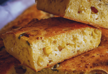 Tranche de pain de maïs mexicain doré, garnie de grains de maïs et de morceaux de jalapenos, avec une texture moelleuse.