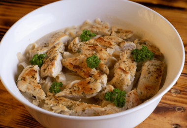 Pâtes crémeuses au poulet et au Boursin, garnies de persil frais, servies dans une assiette blanche.