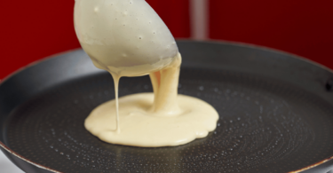 Pâte à crêpes lisse et onctueuse dans un bol, avec une louche prête à l'emploi pour des crêpes fines et dorées.