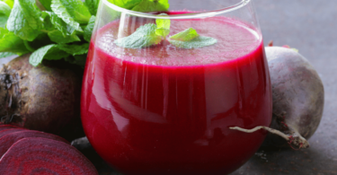 Un verre de jus de betteraves frais, accompagné de morceaux de betteraves crues et de rondelles de citron.