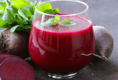 Un verre de jus de betteraves frais, accompagné de morceaux de betteraves crues et de rondelles de citron.