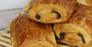 Petits pains au chocolat dorés et feuilletés sortant du four, posés sur une plaque