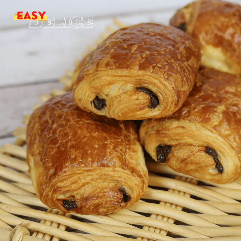 Petits pains au chocolat dorés et feuilletés sortant du four, posés sur une plaque