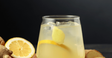 Une boisson detox au citron et gingembre servie dans un verre avec des rondelles de citron et des morceaux de gingembre