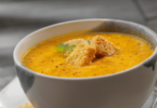 Bol de soupe de carottes onctueuse, garnie de crème fraîche et de quelques brins de coriandre.