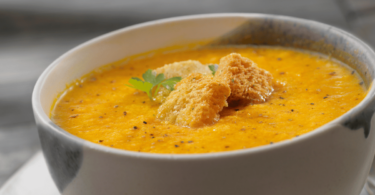 Bol de soupe de carottes onctueuse, garnie de crème fraîche et de quelques brins de coriandre.