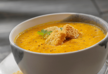 Bol de soupe de carottes onctueuse, garnie de crème fraîche et de quelques brins de coriandre.