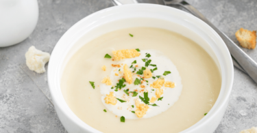 Bol de soupe de chou-fleur crémeuse, décorée de croutons dorés et d’un filet d’huile d’olive.