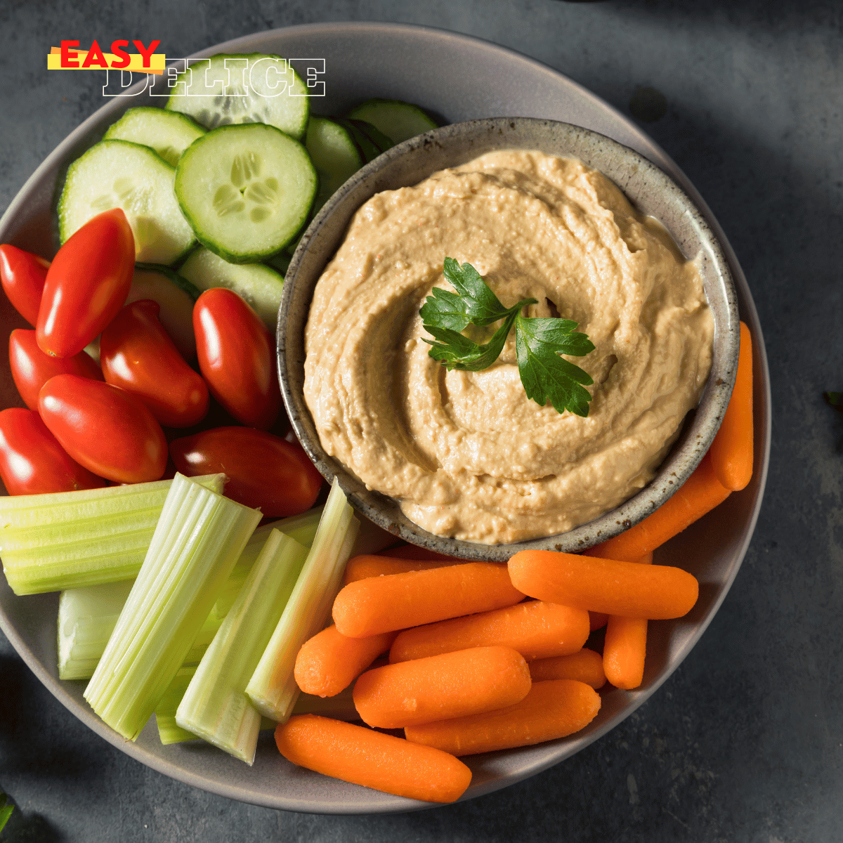 Assiette de collations santé avec des bâtonnets de légumes, du houmous, et un smoothie aux fruits rouges.