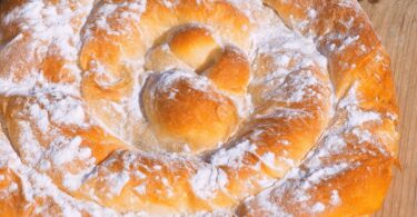 Ensaïmada dorée et saupoudrée de sucre glace, servie sur un plateau rustique.