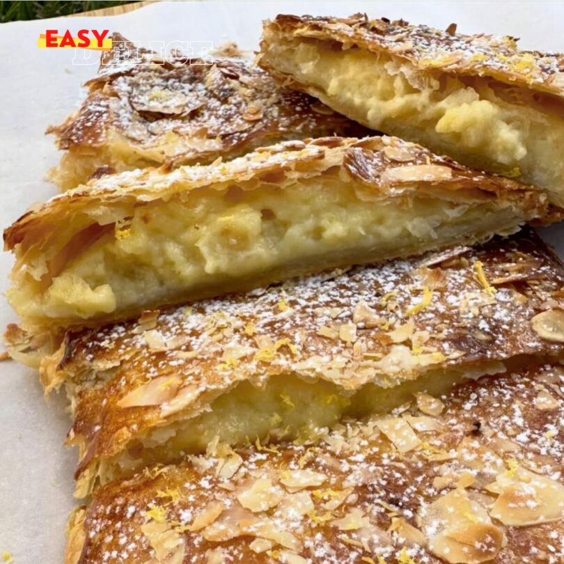 Feuilleté au citron doré, saupoudré de sucre glace et garni de zestes de citron, servi sur une assiette élégante.