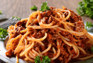 Spaghettis bolognaise servis dans un plat, garnis de parmesan et de persil frais.