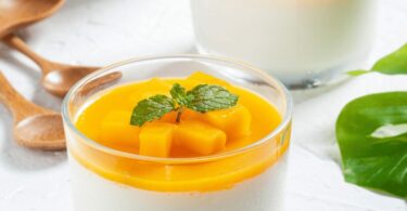 Verrine de panna cotta à la mangue, surmontée de purée de mangue fraîche, décorée de feuilles de menthe.