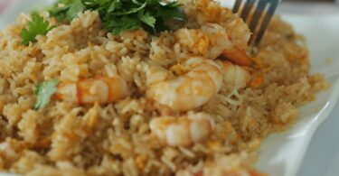 Riz sauté thaï aux légumes et crevettes servi dans un bol avec des herbes fraîches.