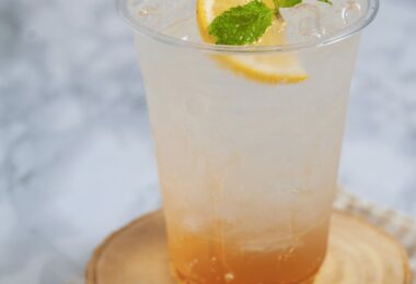 Verre de soda au miel et citron, garni de rondelles de citron et de feuilles de menthe, servi avec des glaçons.