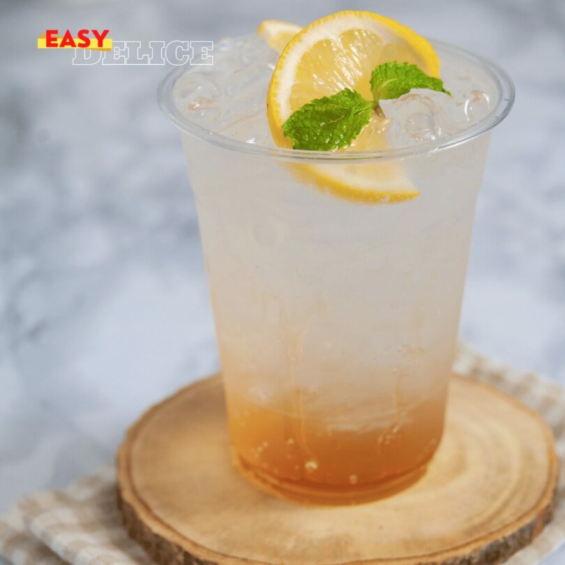 Verre de soda au miel et citron, garni de rondelles de citron et de feuilles de menthe, servi avec des glaçons.