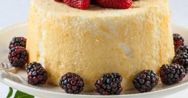 Gâteau des anges aérien, tranché, accompagné d’un coulis de fruits rouges et de menthe fraîche.