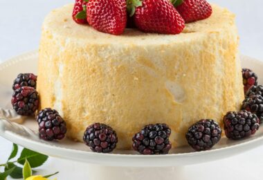 Gâteau des anges aérien, tranché, accompagné d’un coulis de fruits rouges et de menthe fraîche.