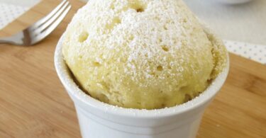 Mugcake au citron doré, moelleux et servi avec du sucre glace et des zestes de citron.