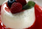 Panna cotta onctueuse dans une verrine, nappée de coulis de fruits rouges et décorée avec une feuille de menthe.