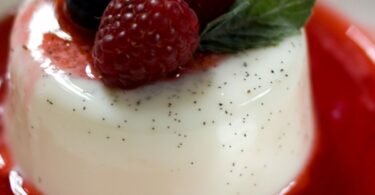 Panna cotta onctueuse dans une verrine, nappée de coulis de fruits rouges et décorée avec une feuille de menthe.