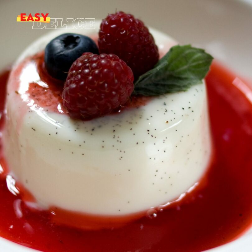 Panna cotta onctueuse dans une verrine, nappée de coulis de fruits rouges et décorée avec une feuille de menthe.