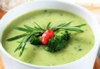 Bol de velouté de brocoli et truite garni de persil frais sur une table rustique.