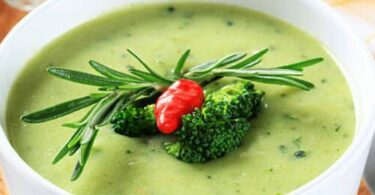 Bol de velouté de brocoli et truite garni de persil frais sur une table rustique.