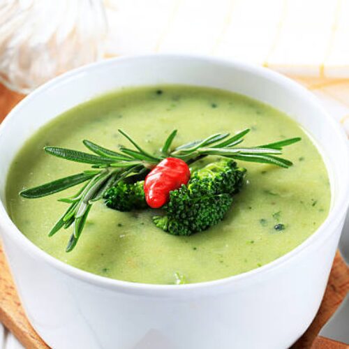 Bol de velouté de brocoli et truite garni de persil frais sur une table rustique.