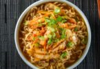 Bol de soupe aux nouilles ramen avec poulet, œuf mollet et oignons verts sur une table en bois.