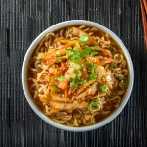 Bol de soupe aux nouilles ramen avec poulet, œuf mollet et oignons verts sur une table en bois.