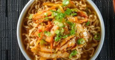 Bol de soupe aux nouilles ramen avec poulet, œuf mollet et oignons verts sur une table en bois.