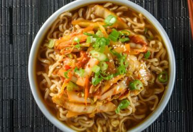 Bol de soupe aux nouilles ramen avec poulet, œuf mollet et oignons verts sur une table en bois.