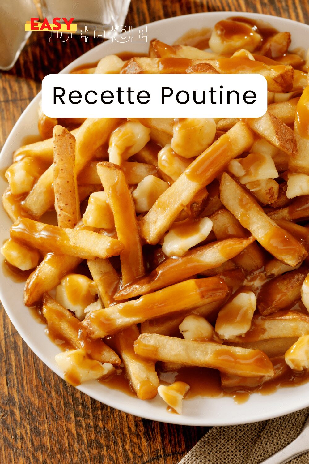 Poutine québécoise servie dans une assiette avec des frites dorées, du fromage en grains et une sauce brune nappante.