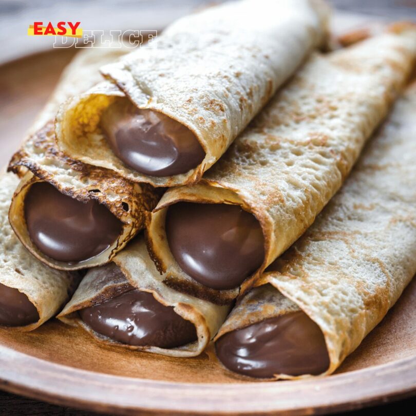 Crêpes dorées garnies de Nutella et pliées sur une assiette avec une touche de sucre glace.