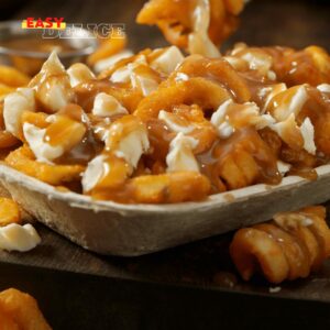 Poutine québécoise servie dans une assiette avec des frites dorées, du fromage en grains et une sauce brune nappante.