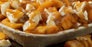 Poutine québécoise servie dans une assiette avec des frites dorées, du fromage en grains et une sauce brune nappante.