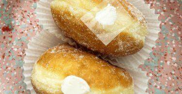 Beignets à la crème pâtissière vanille et chocolat saupoudrés de sucre et cacao sur une assiette.